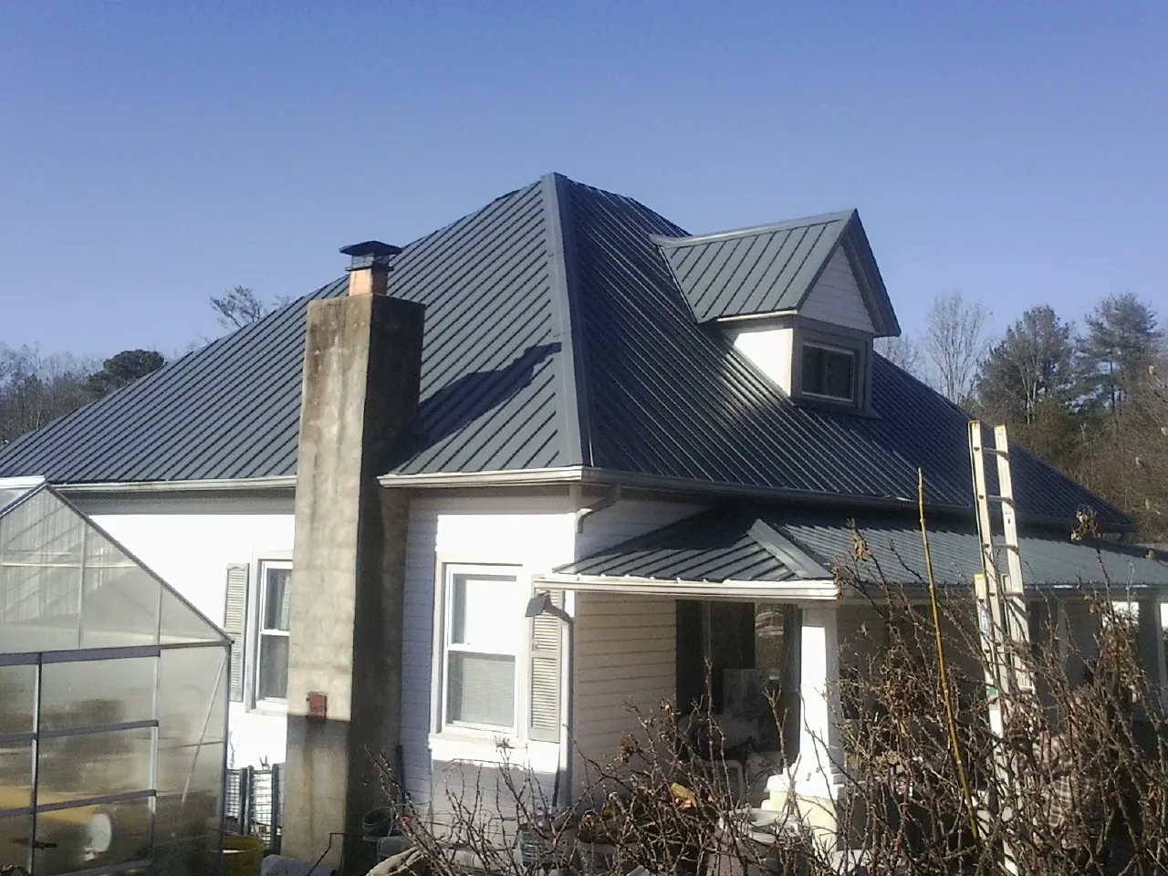 Dark blue standing seam metal roof on a white farmhouse with dormer — Slate & Tile Roof Repair by Roofing Brothers in Germanton