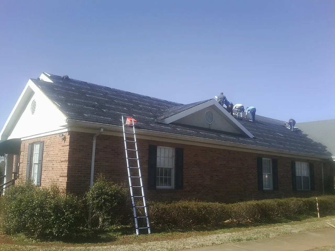 Crew tearing shingles off a brick ranch roof with a ladder set — Metal Roof Repair work by our crew in Germanton