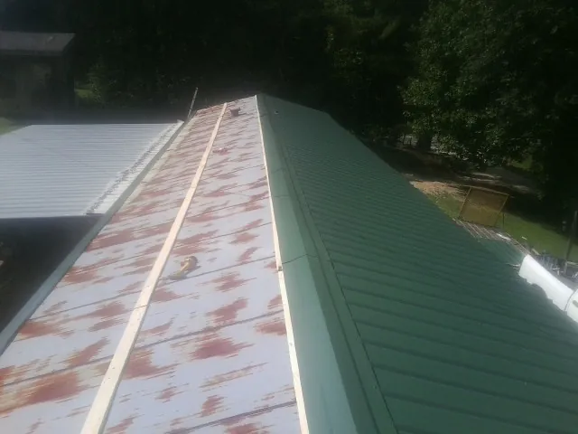 Old rusted panels beside newly installed green metal roofing — Wind Damage Roof Repair by Roofing Brothers in Germanton