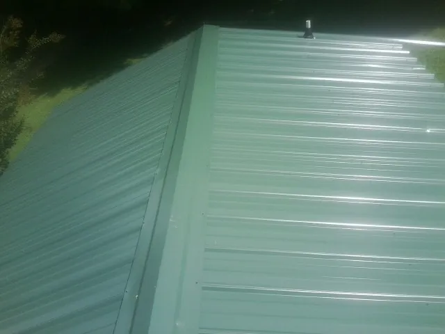 New green metal panels meeting at the ridge of a roof — Flat Roof Repair work by our crew in Germanton