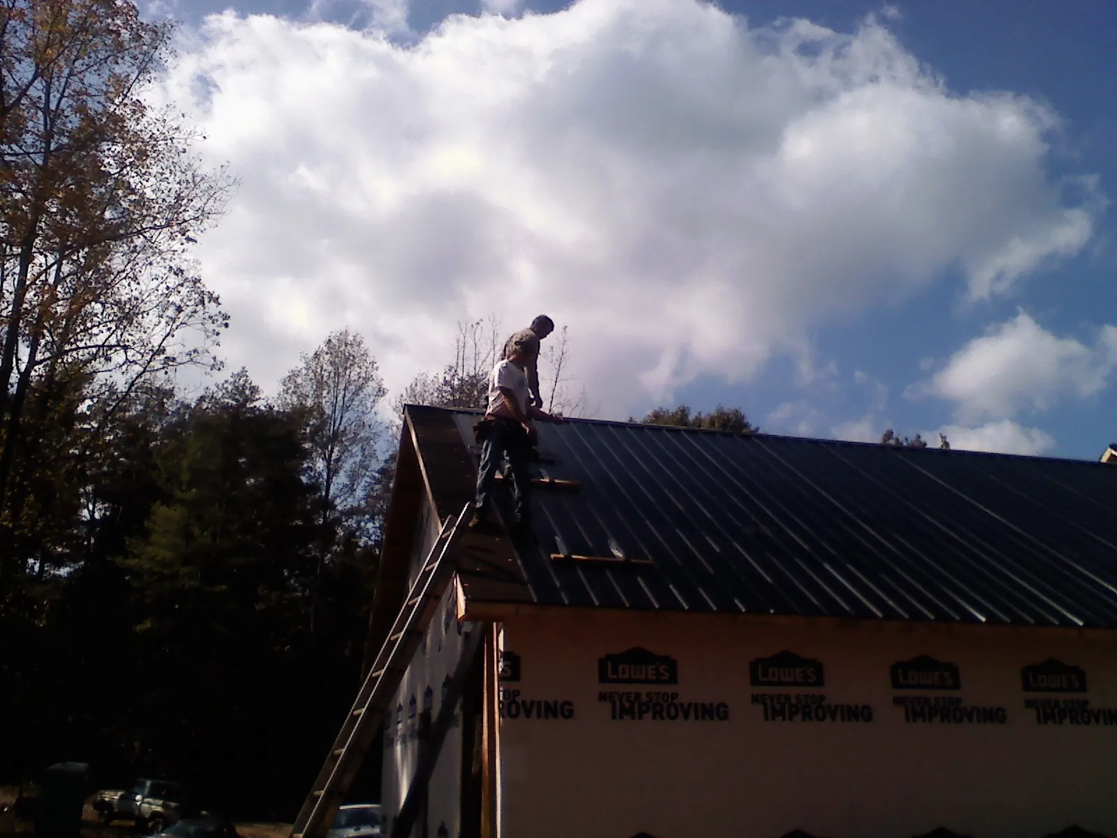 Roofer fastening dark metal panels high against a cloudy sky, from a Roof Inspection job in Germanton