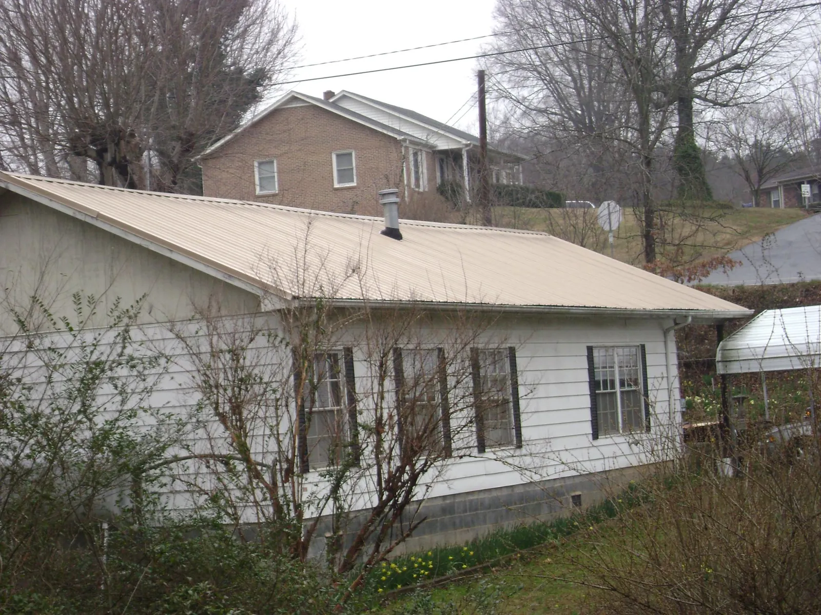 Tan metal roof on a white sided house set into a hillside — Commercial Roofing by Roofing Brothers in Germanton