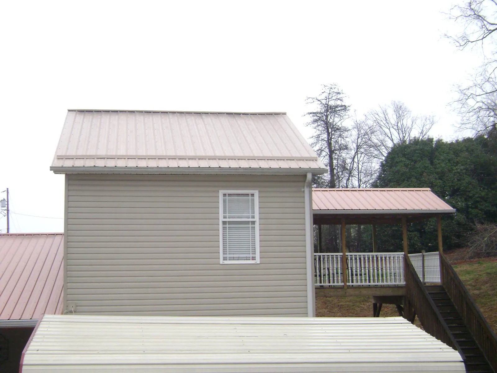 Tan metal roofs on a two story addition and attached porch, from a Roof Replacement job in Germanton